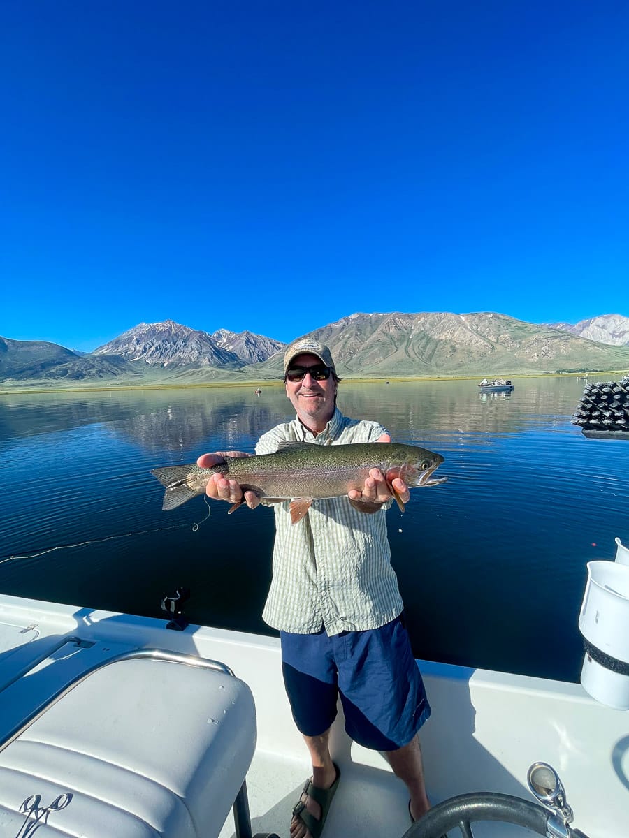 A fisherman holding a large rainbow trout from Crowley Lake on a boat.