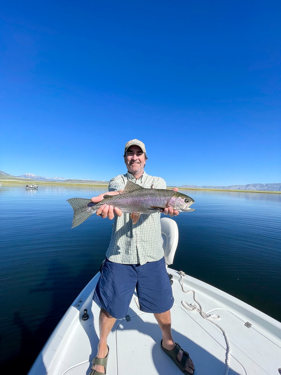 A fisherman holding a large rainbow trout from Crowley Lake on a boat.