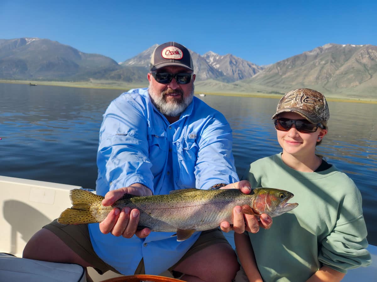 A fisherman holding a large rainbow trout from Crowley Lake on a boat.