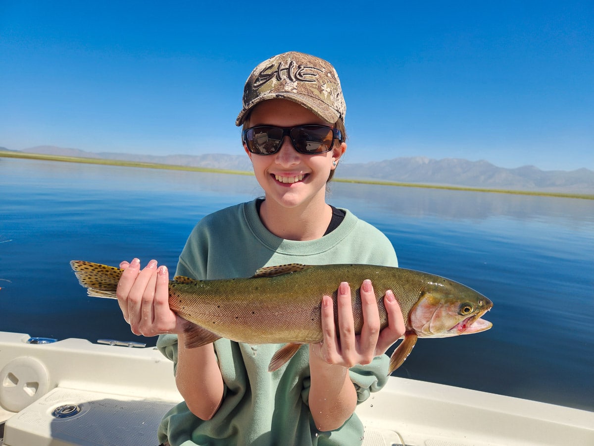 A fisherman holding a large cutthroat trout from Crowley Lake on a boat.