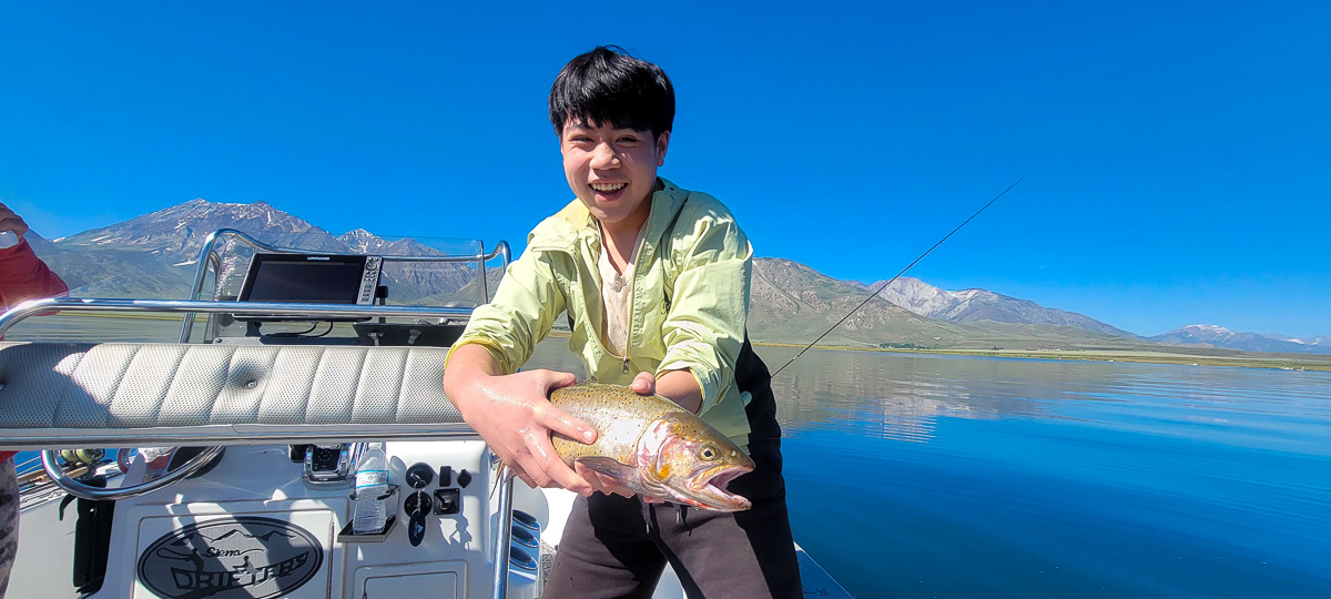 A fisherman holding a large cutthroat trout from Crowley Lake on a boat.