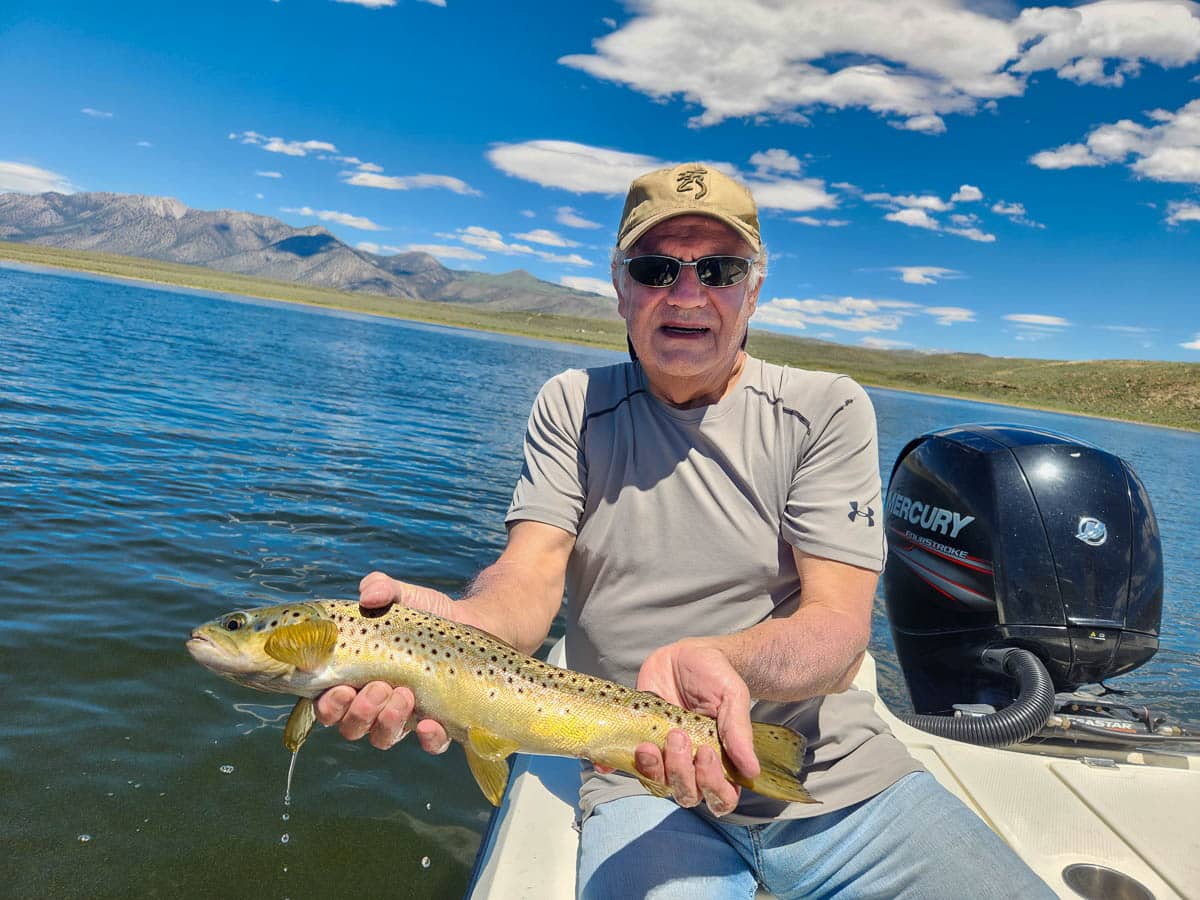 A fisherman holding a large brown trout from Crowley Lake on a boat.