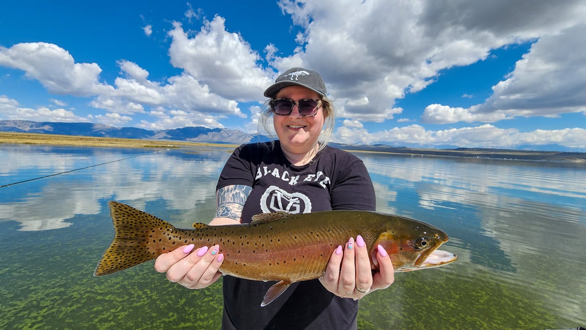 A fisherwoman holding a large cutthroat trout from Crowley Lake on a boat.