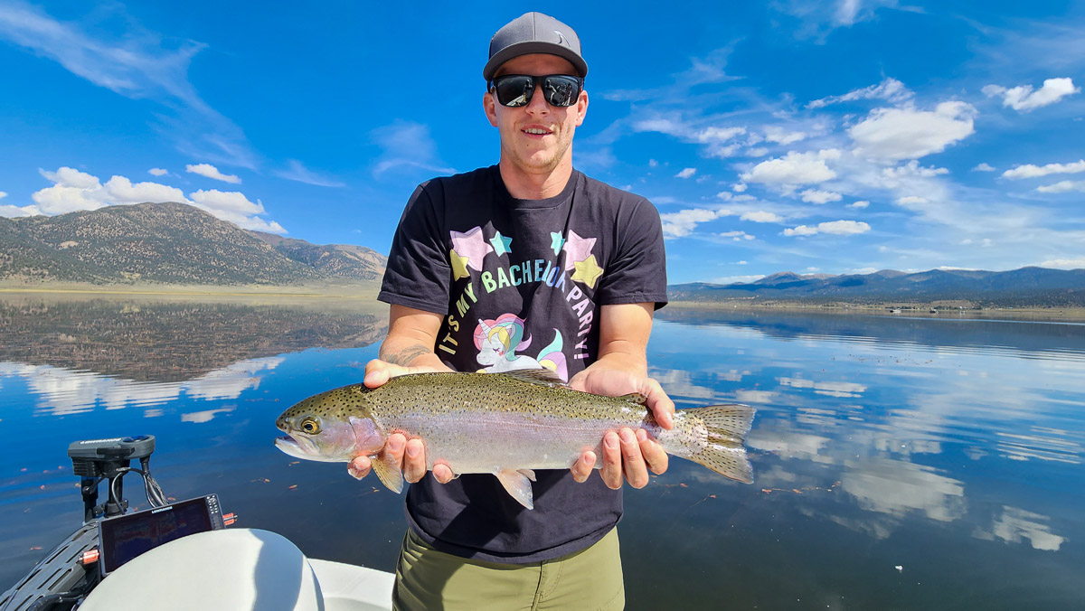 A fisherman holding a large rainbow trout from Bridgeport Reservoir on a boat.