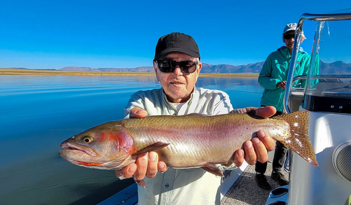 A fisherman holding a large cutthroat trout from Crowley Lake on a boat.