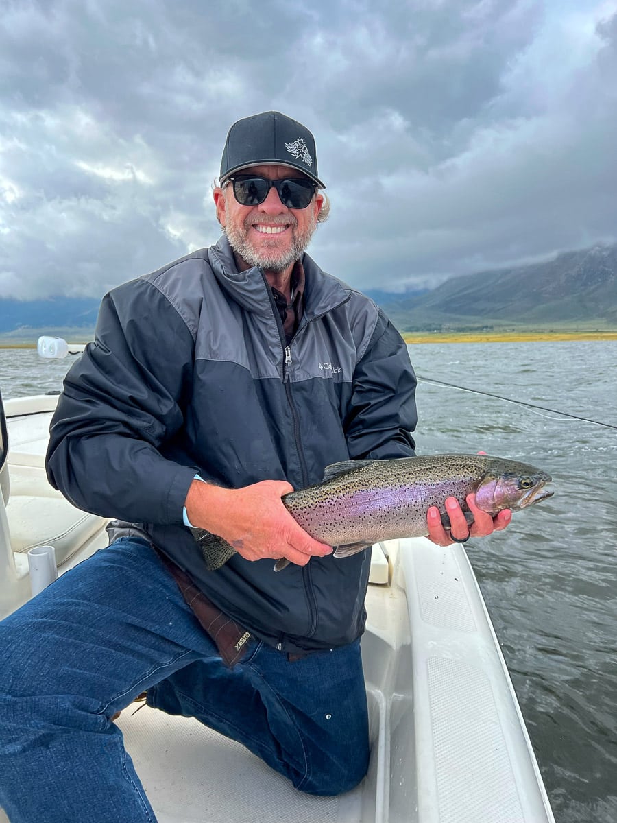 A fisherman holding a large rainbow trout from Crowley Lake on a boat.