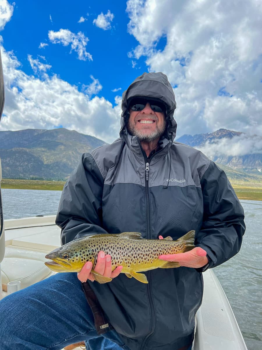 A fisherman holding a large brown trout from Crowley Lake on a boat.