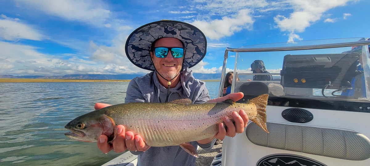 A fisherman holding a large cutthroat trout from Crowley Lake on a boat.