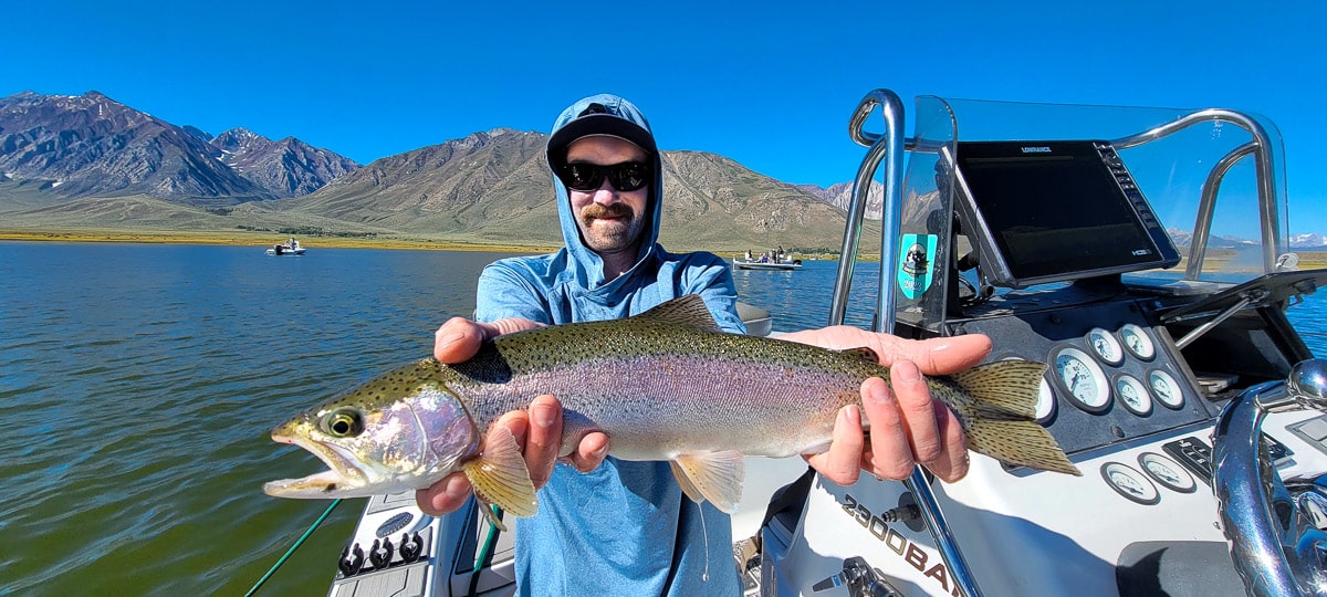 A fisherman holding a large rainbow trout from Crowley Lake on a boat.