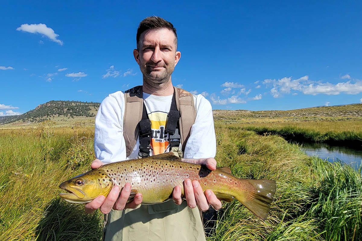 A fisherman holding a large brown trout from Hot Creek.