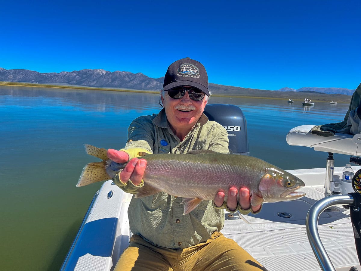 A fisherman holding a large cutthroat trout from Crowley Lake on a boat.