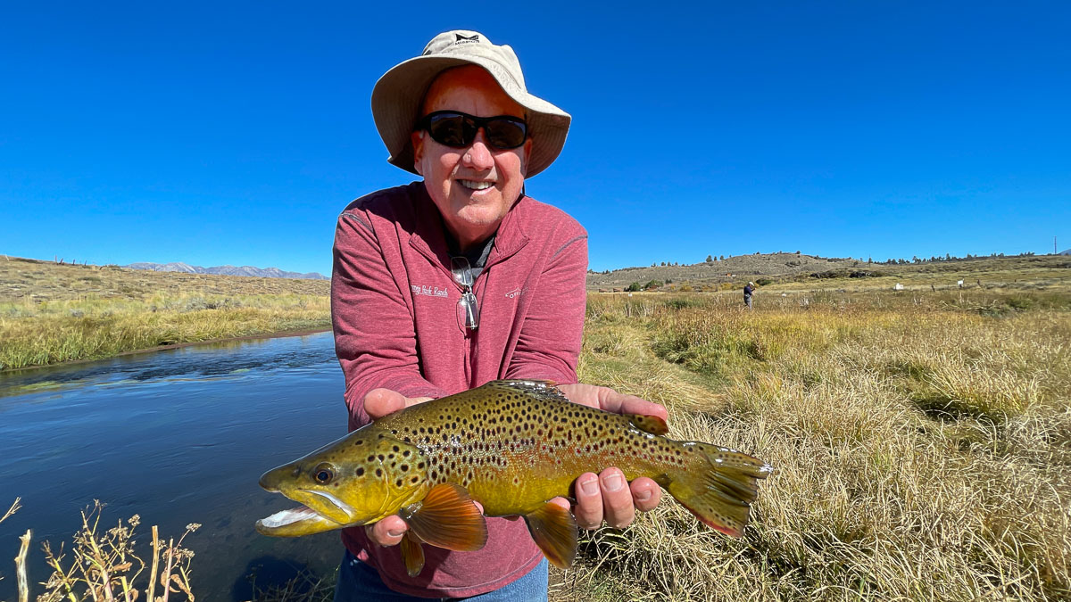 A fisherman holding a large brown trout from Hot Creek.