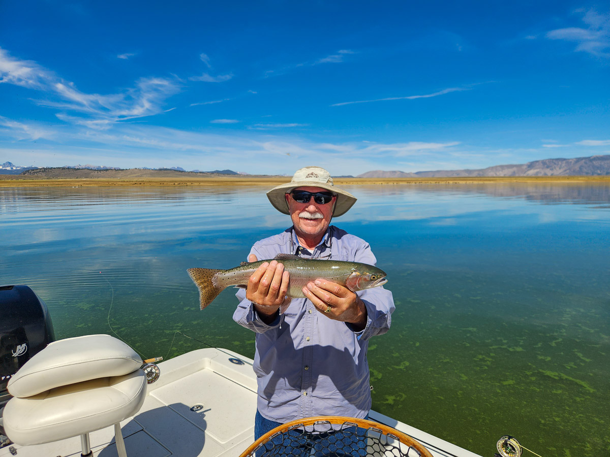A fisherman holding a large cutthroat trout from Crowley Lake on a boat.