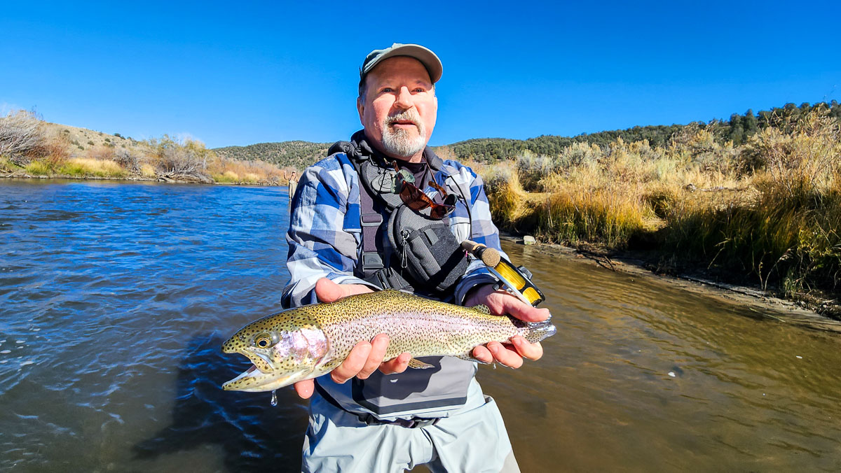 A smiling fisherman holding a large rainbow trout on the East Walker River.