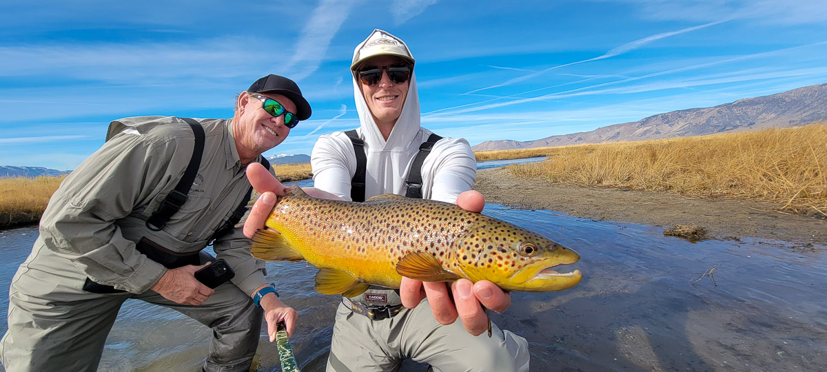 A smiling fisherman holding a large brown trout on the Upper Owens River.
