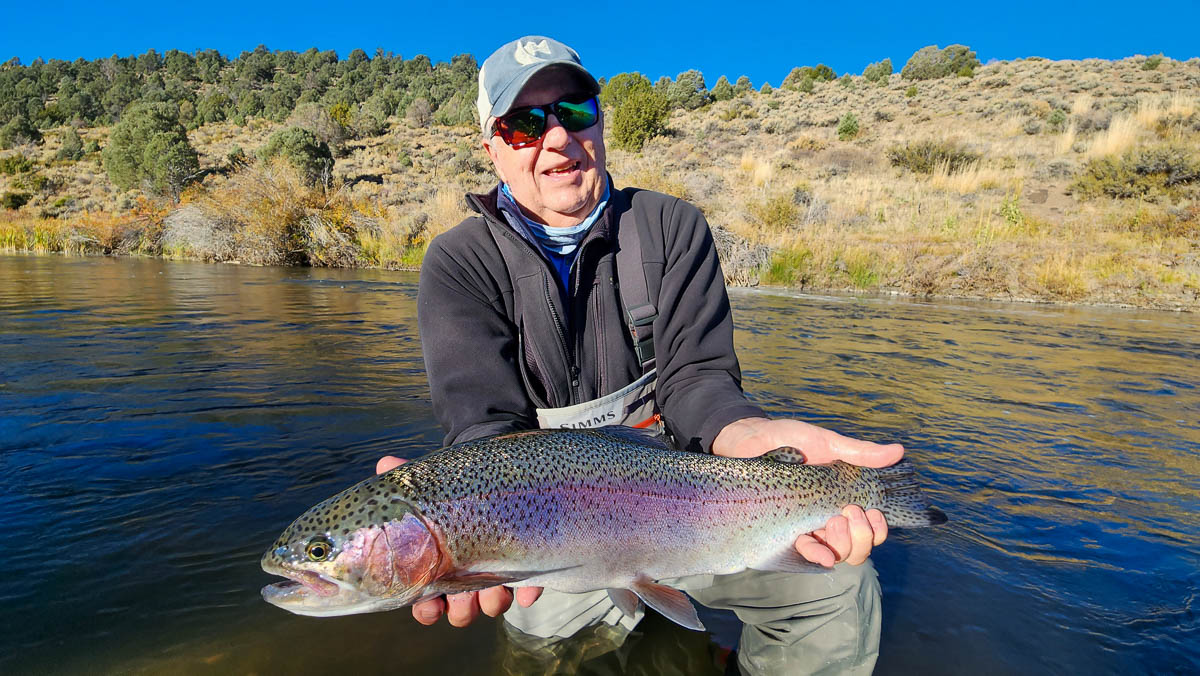 A smiling fisherman holding a large rainbow trout on the East Walker River