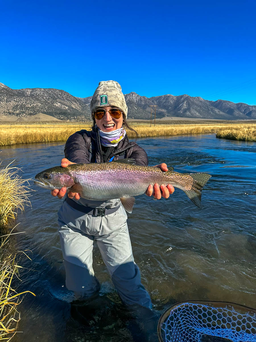 A smiling fisherwoman holding a large rainbow trout on the Upper Owens River.