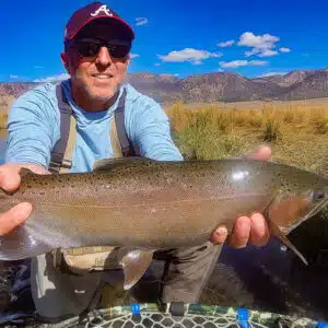 An orange colored sky glows from a winter morning sunrise in Crowley Lake with freshly fallen snow on the ground.
