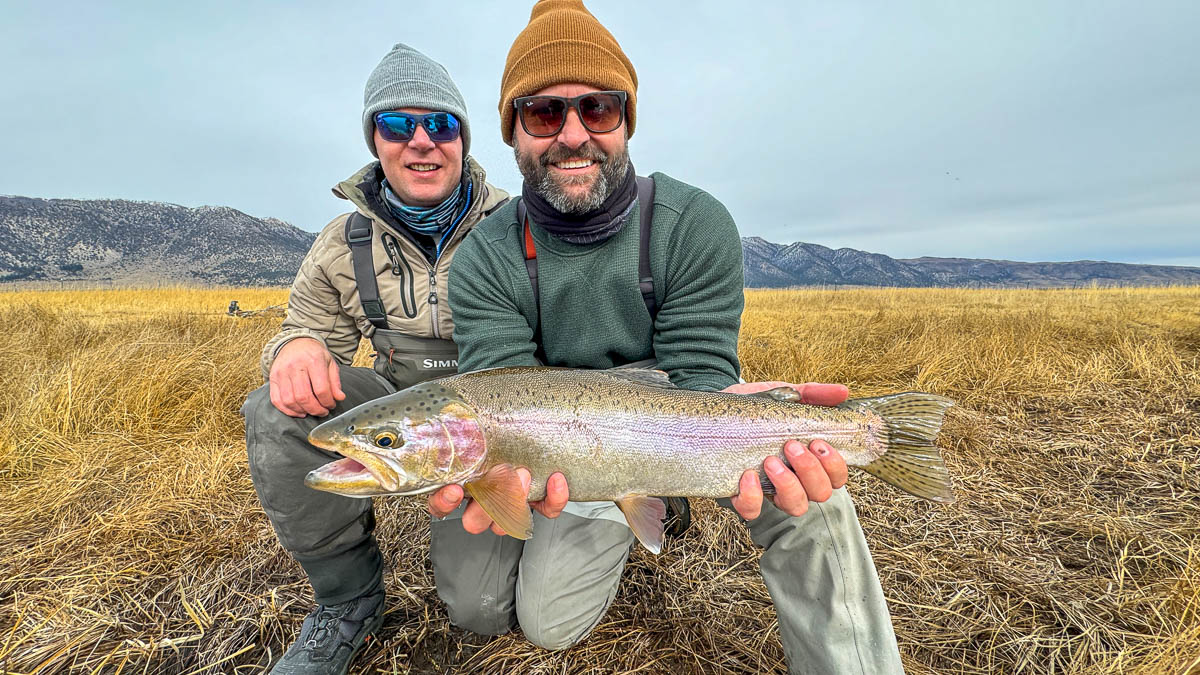 A smiling fisherman holding a large rainbow trout on the Upper Owens River.