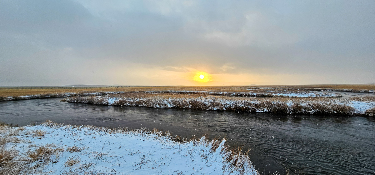 A rising sun shining through the clouds of a snowstorm on the Upper Owens River in the eastern sierra.