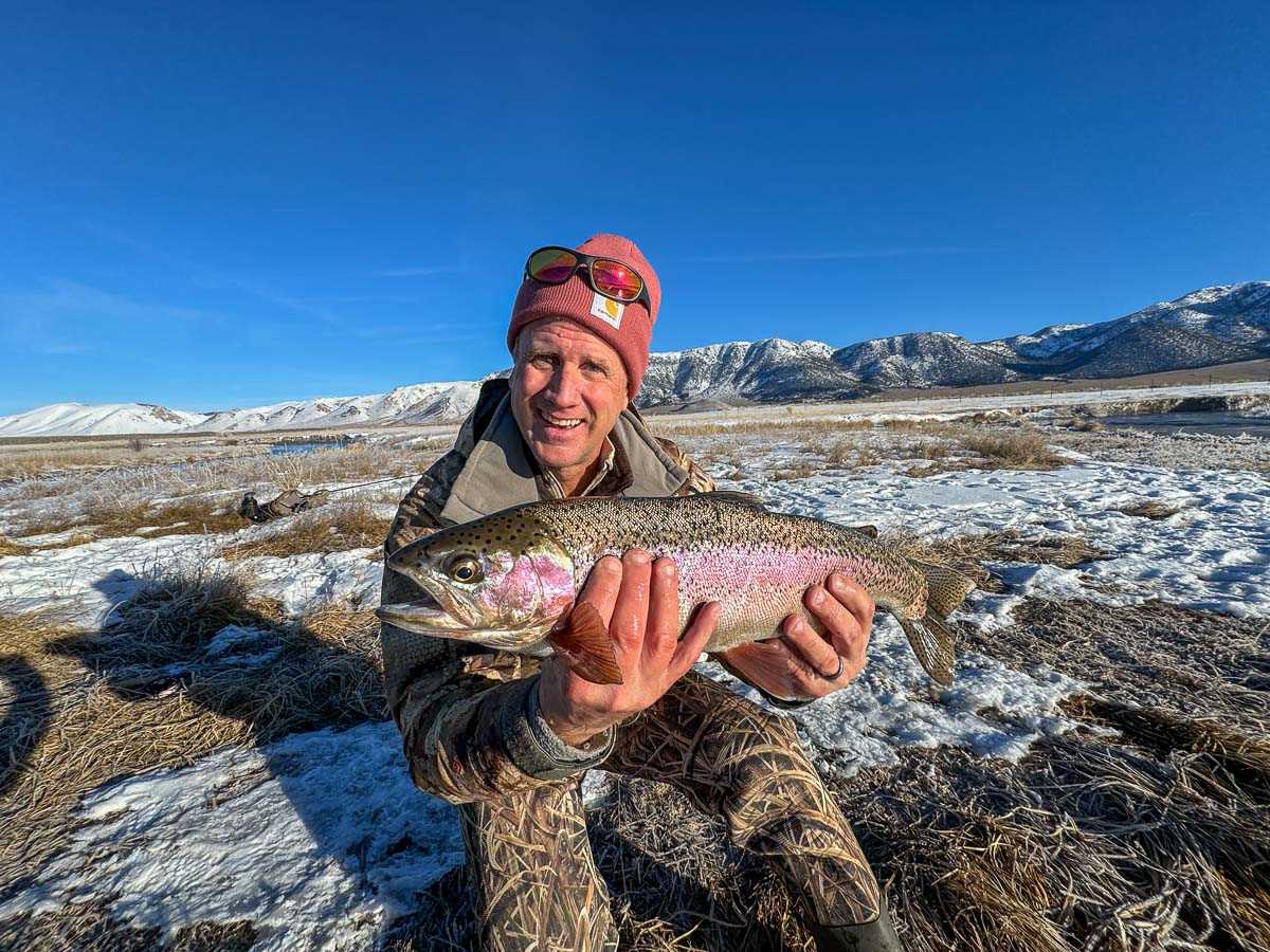 A smiling fisherman holding a large rainbow trout on the Upper Owens River.