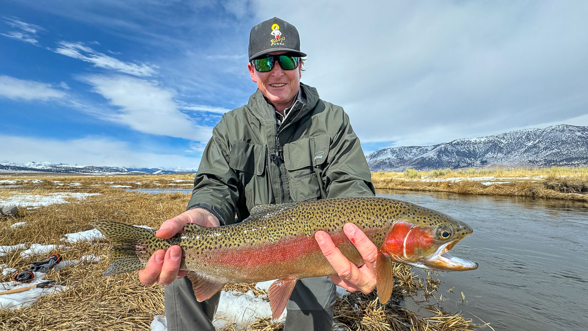 A smiling fisherman holding a large brown trout on the Upper Owens River.