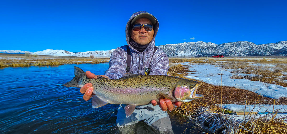 A smiling fisherman holding a rainbow trout on the Upper Owens River.