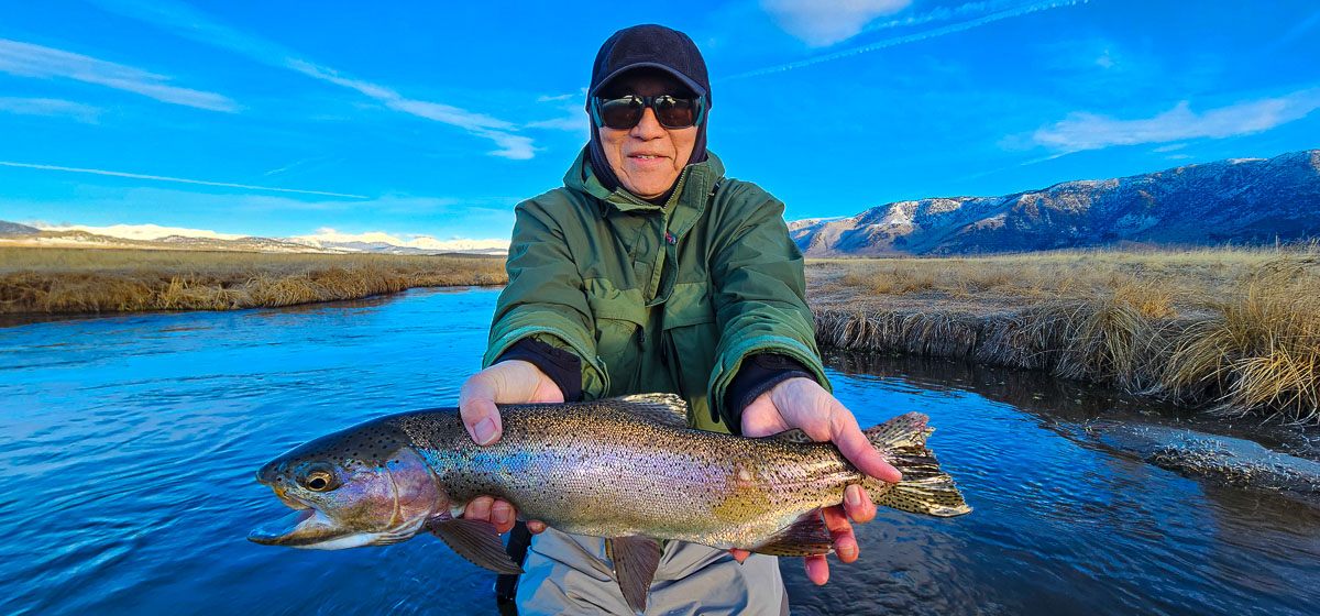 A smiling fisherman holding a large rainbow trout on the Upper Owens River