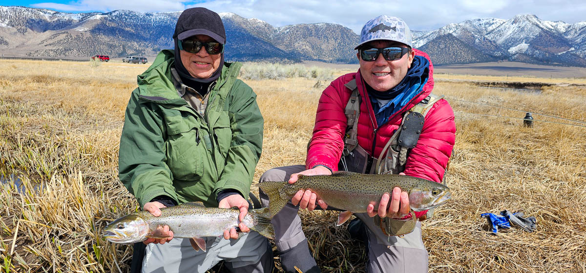 A smiling pair fisherman holding a couple large rainbow trout on the Upper Owens River.