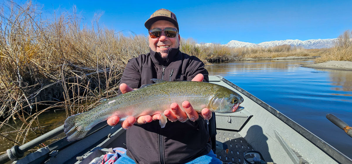 A smiling angler holding a rainbow trout in a drift boat on the Lower Owens River.