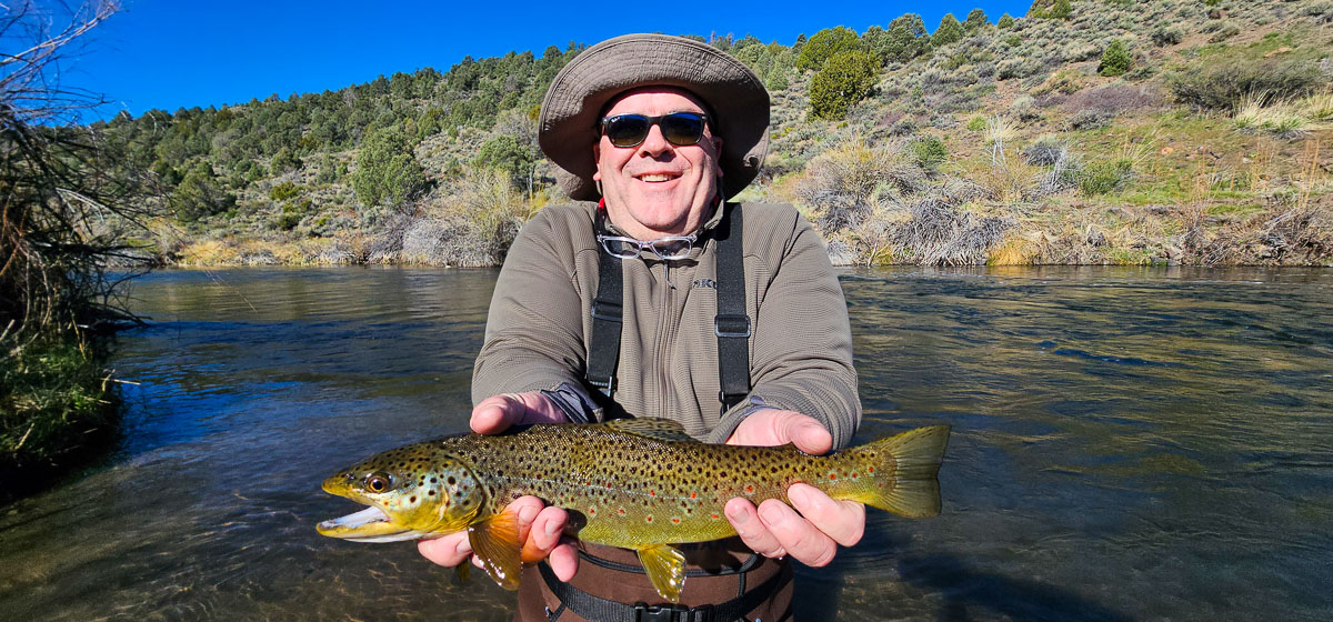 A smiling angler with a wide brim hat holding a large brown trout on the East Walker River.