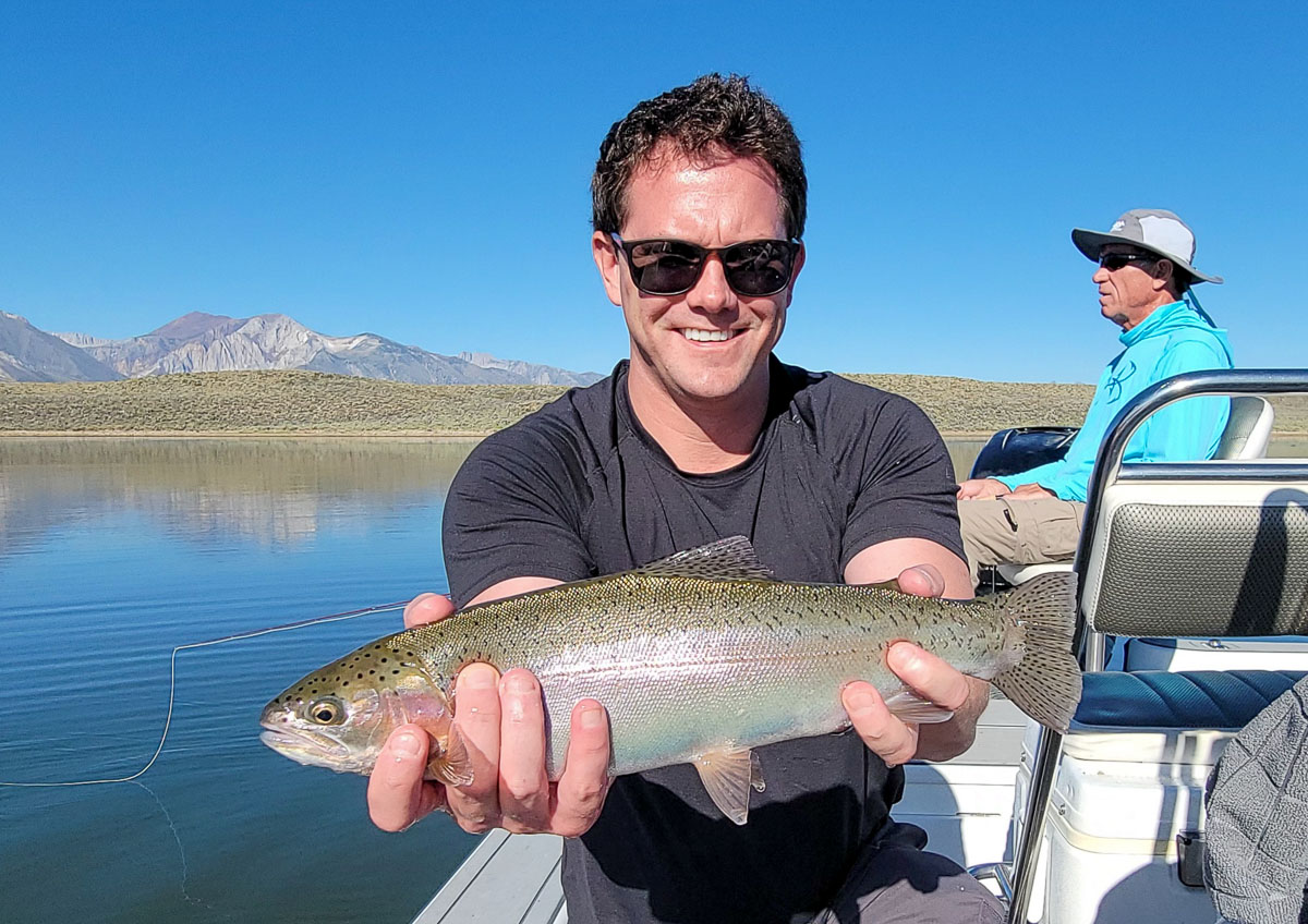 A fly fishermen holding a large rainbow trout in a boat on Crowley Lake in the Eastern Sierra.