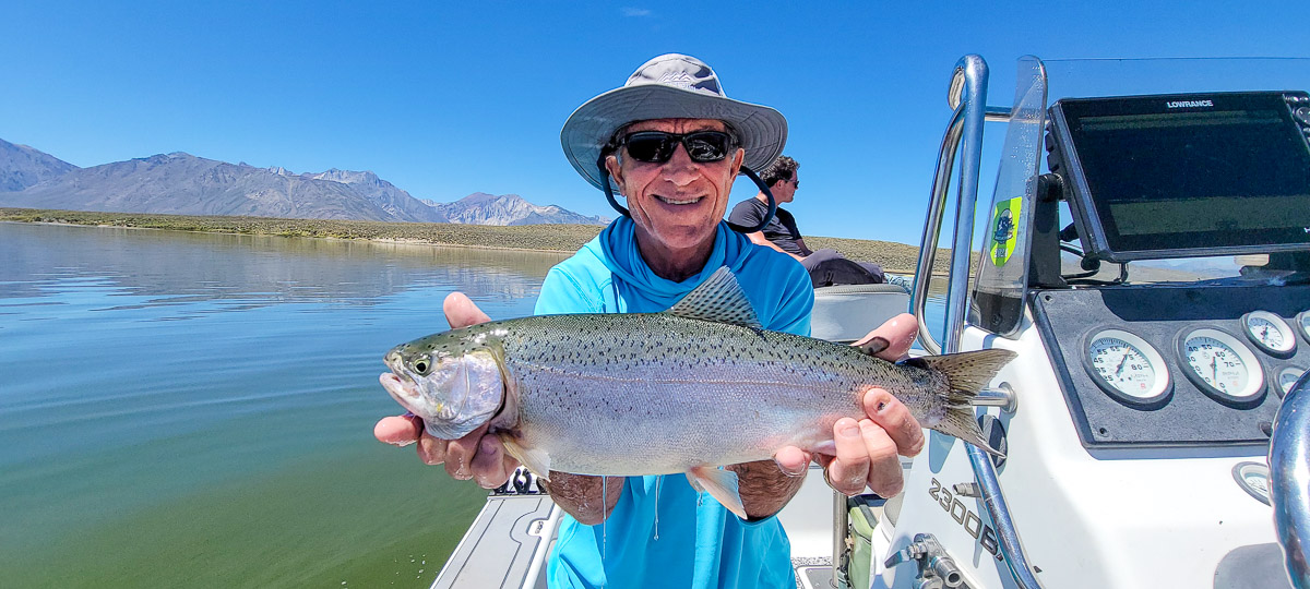 A fly fishermen holding a large rainbow trout in a boat on Crowley Lake in the Eastern Sierra.