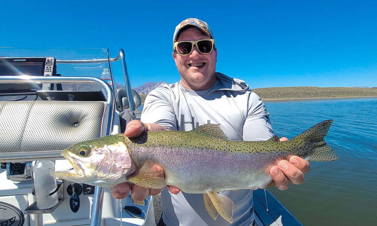 A fly fishermen holding a large rainbow trout in a boat on Crowley Lake in the Eastern Sierra.