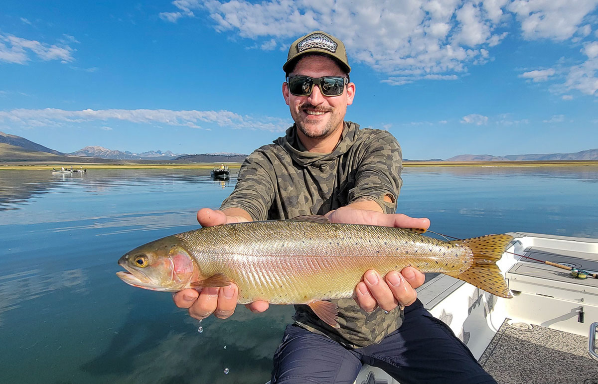 A fly fishermen holding a large cutthroat trout in a boat on Crowley Lake in the Eastern Sierra.