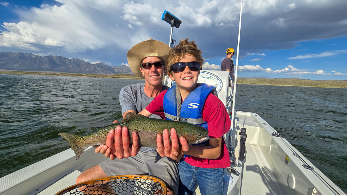 A fly fishermen holding a large rainbow trout in a boat on Crowley Lake in the Eastern Sierra.