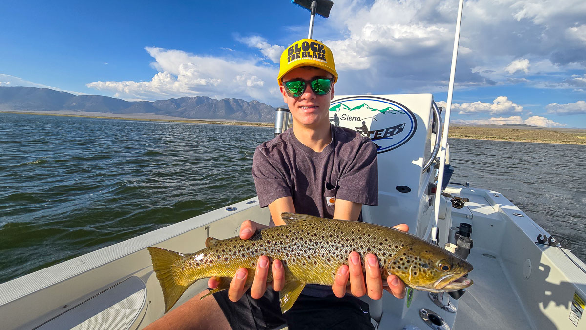 A fly fishermen holding a large brown trout in a boat on Crowley Lake in the Eastern Sierra.