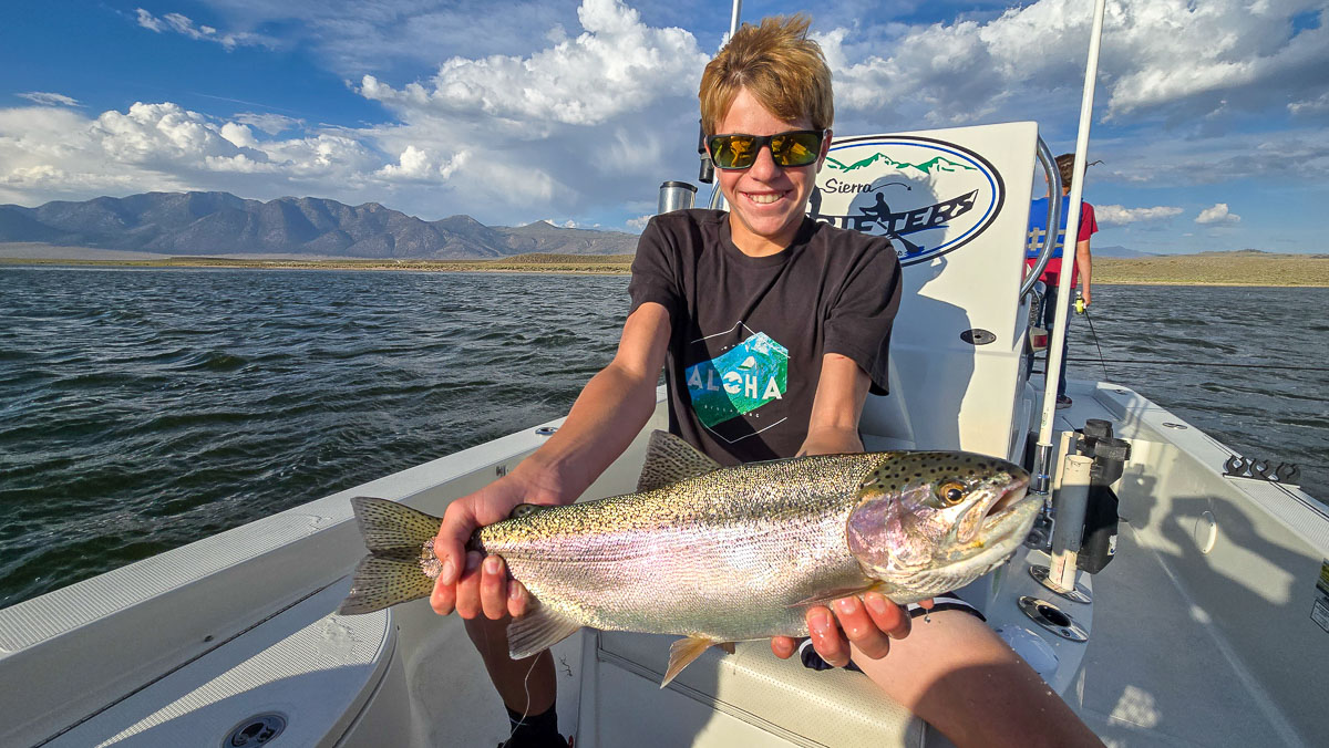 A fly fishermen holding a large rainbow trout in a boat on Crowley Lake in the Eastern Sierra.