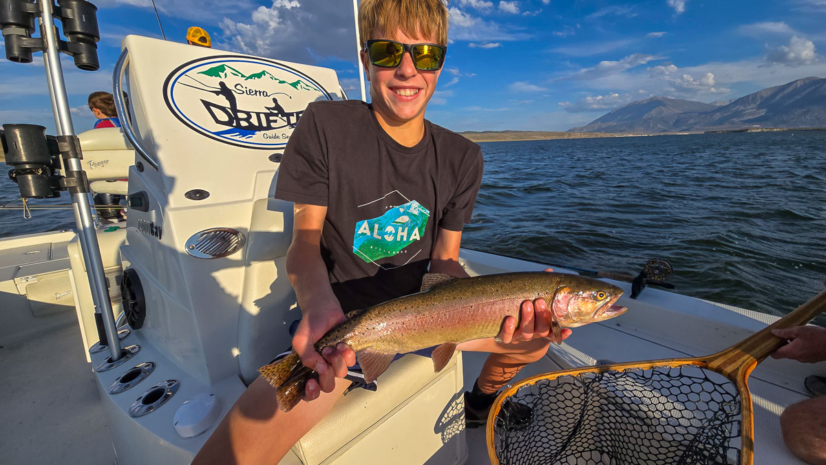 A fly fishermen holding a large cutthroat trout in a boat on Crowley Lake in the Eastern Sierra.