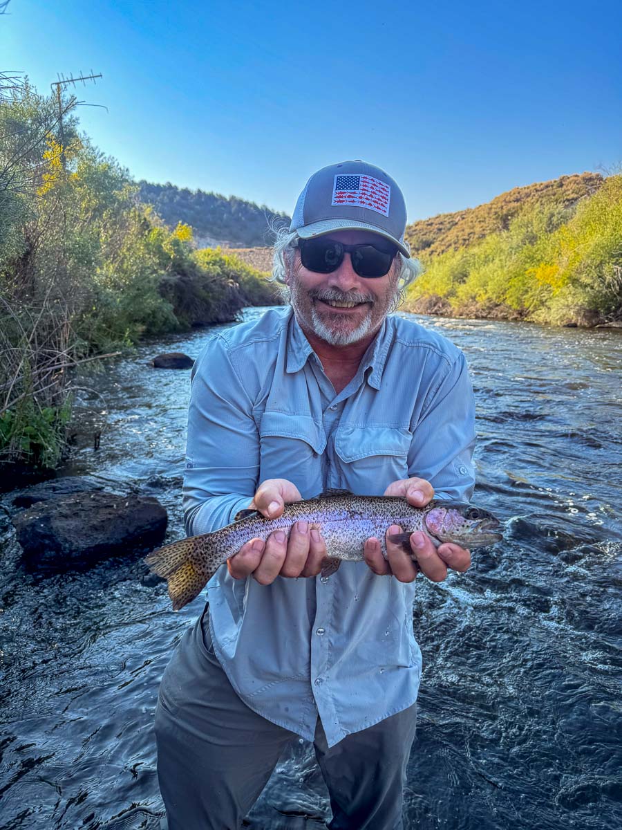 A fly fisherman holding a rainbow trout on the East Walker River in Bridgeport, CA.