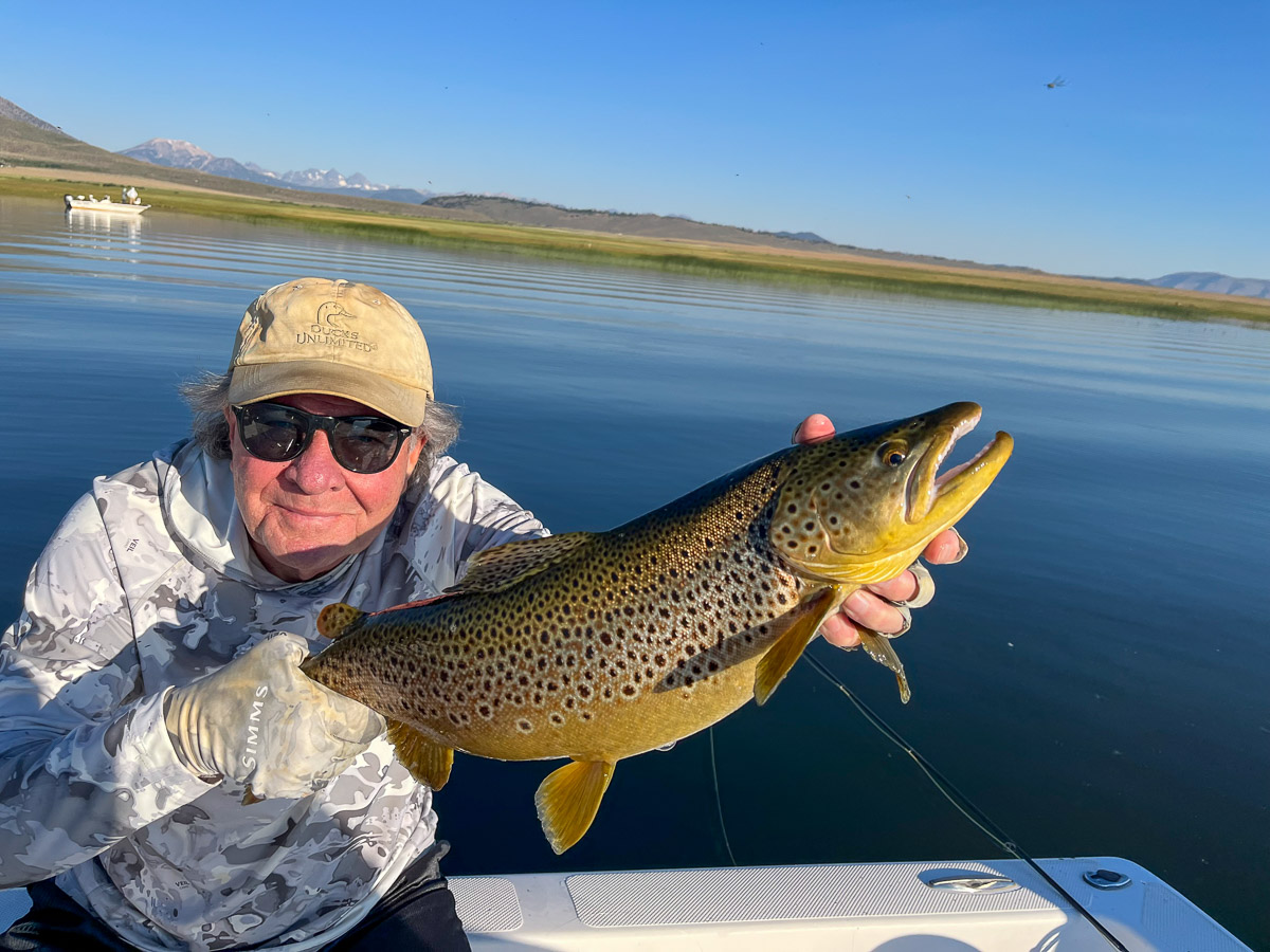 A fly fishermen holding a larger rainbow trout in a boat on Crowley Lake in the Eastern Sierra.