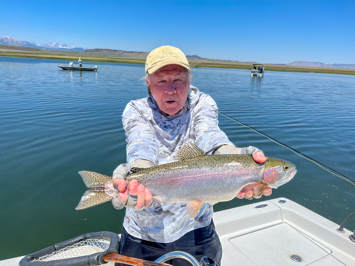 A fly fishermen holding a larger rainbow trout in a boat on Crowley Lake in the Eastern Sierra.