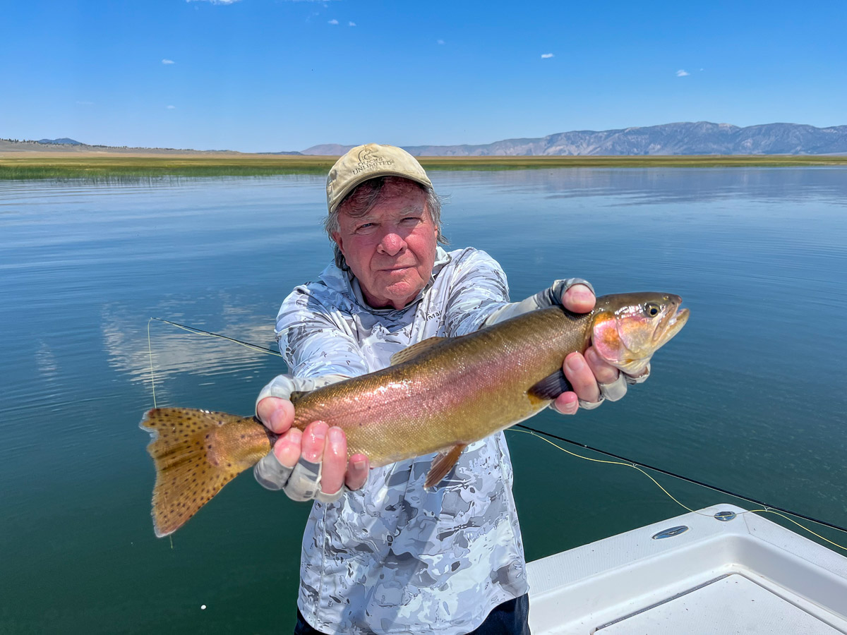 A fly fishermen holding a larger rainbow trout in a boat on Crowley Lake in the Eastern Sierra.