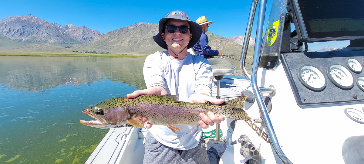 A fly fishermen holding a larger rainbow trout in a boat on Crowley Lake in the Eastern Sierra.