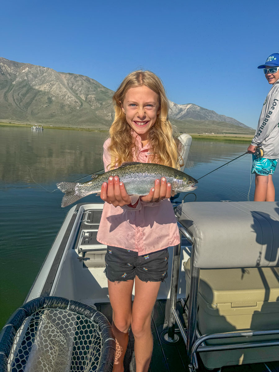 A fly fishermen holding a larger rainbow trout in a boat on Crowley Lake in the Eastern Sierra.