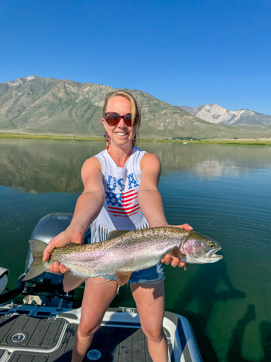 A fly fishermen holding a larger rainbow trout in a boat on Crowley Lake in the Eastern Sierra.