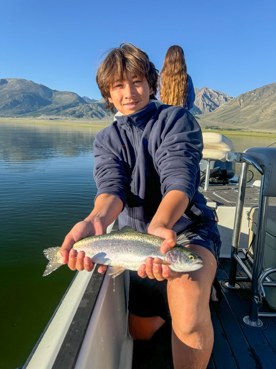 A fly fishermen holding a larger rainbow trout in a boat on Crowley Lake in the Eastern Sierra.