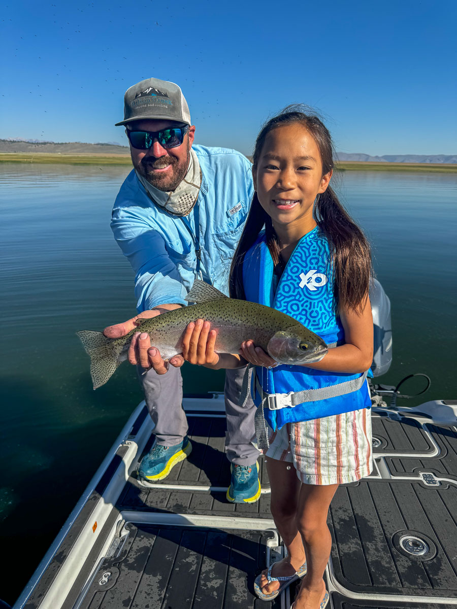 A fly fishermen holding a larger rainbow trout in a boat on Crowley Lake in the Eastern Sierra.