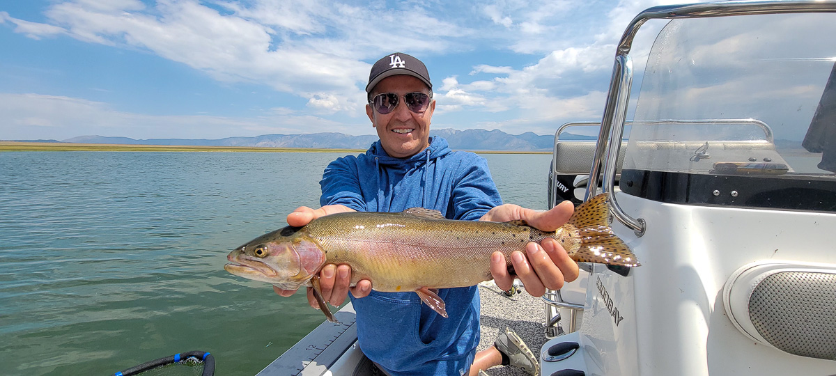 A fly fishermen holding a larger rainbow trout in a boat on Crowley Lake in the Eastern Sierra.