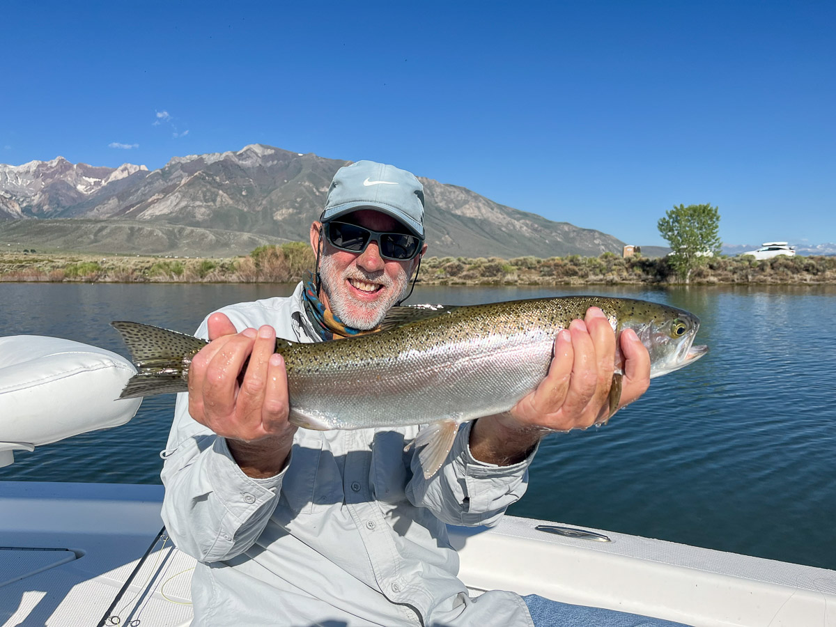 A fly fishermen holding a larger rainbow trout in a boat on Crowley Lake in the Eastern Sierra.